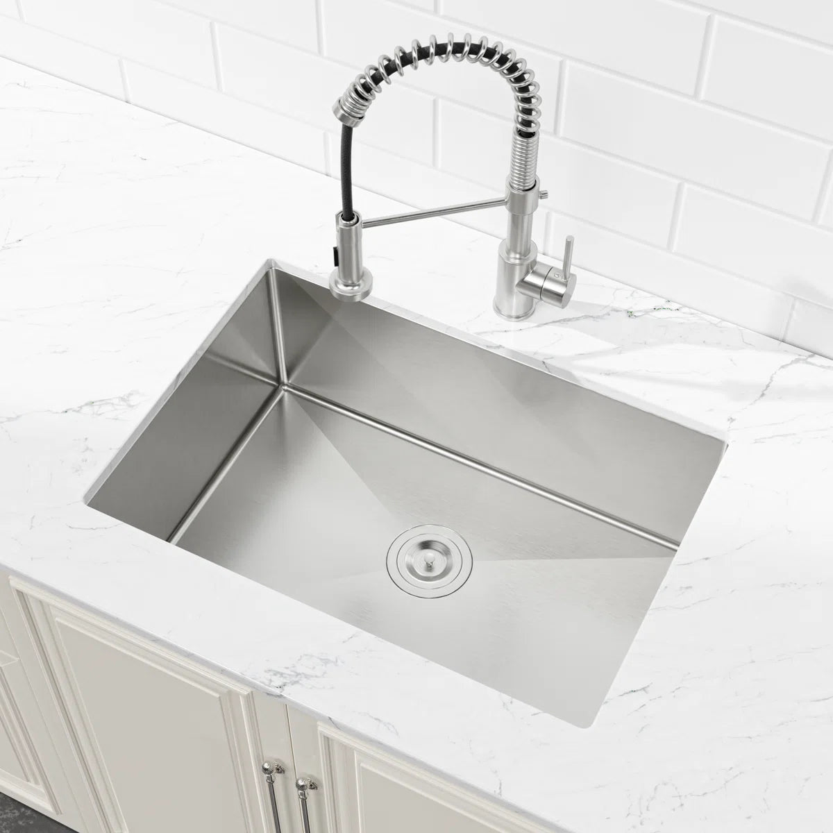 Angled view of Cozy 27-inch brushed nickel undermount single bowl handmade stainless steel kitchen sink installed under white countertop
